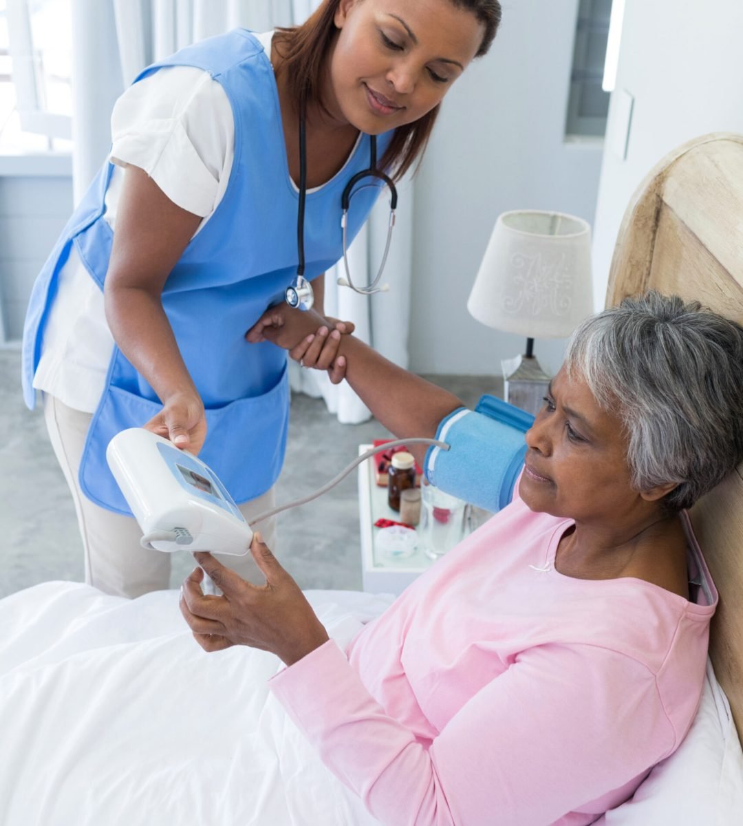 Female doctor measuring blood pressure of senior woman in bedroom